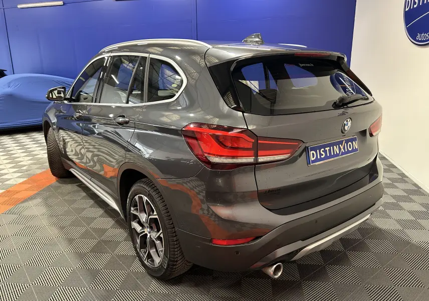 BMW X1 gris en vue 3/4 arrière droit, mettant en valeur son hayon électrique et ses feux arrière LED distinctifs.