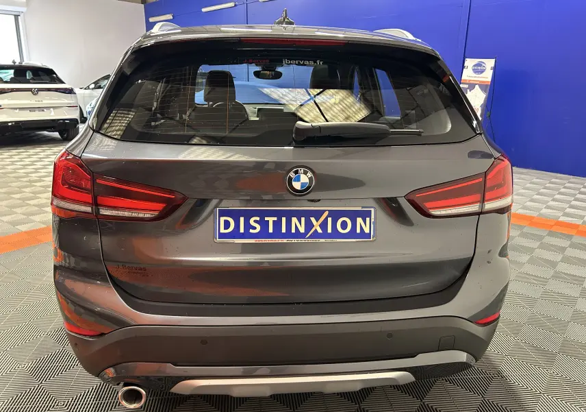Vue arrière d'un BMW X1 gris 2021 avec hayon électrique et logo distinctif du concessionnaire sur plaque.