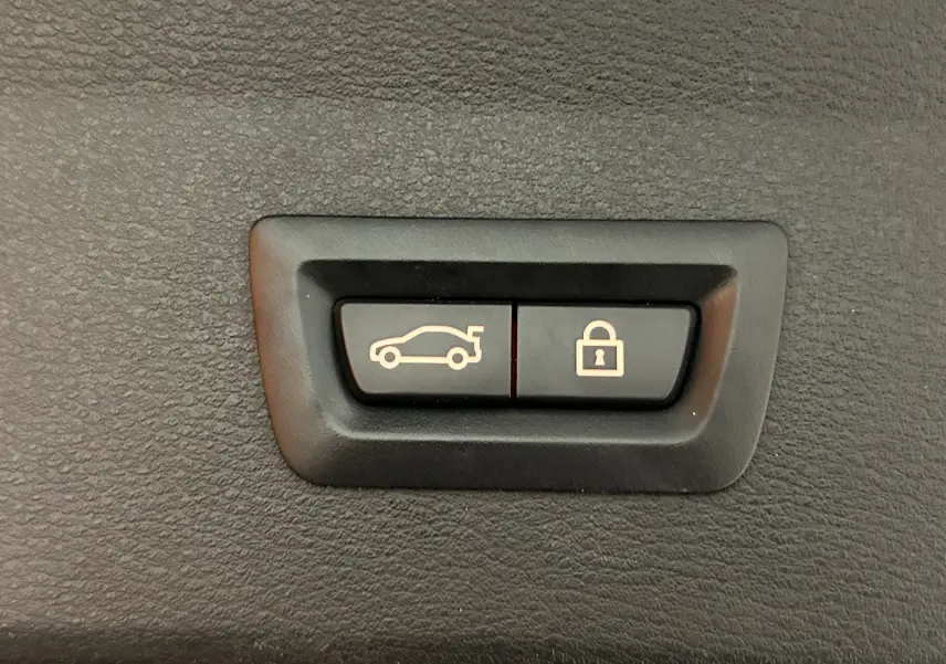 Boutons de commande du hayon électrique et de verrouillage, intégrés dans l'habillage intérieur noir du BMW X1 gris.