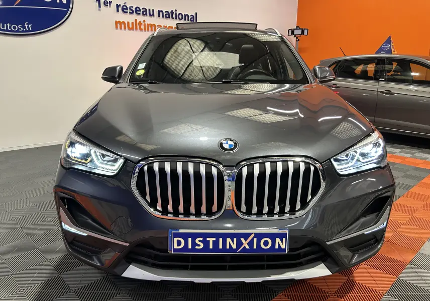 Vue frontale d’un BMW X1 gris avec phares LED allumés et calandre double haricot chromée en showroom.