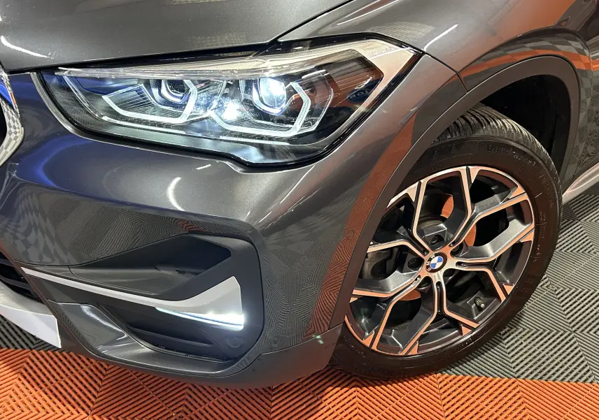 Gros plan sur l'avant droit gris métallisé du BMW X1 avec phare LED allumé et jante alliage distinctive.