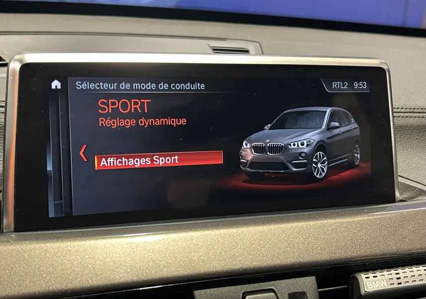 Écran intérieur affichant un mode de conduite Sport avec une image 3/4 avant d'un BMW X1 gris.