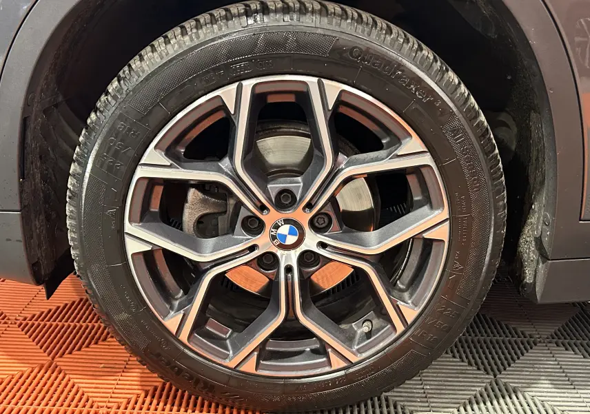 Gros plan sur la roue avant droite d’un BMW X1 gris, mettant en valeur la jante alliage au design moderne et le logo BMW central.