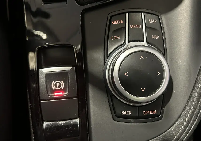Gros plan sur la molette de commande multimédia et le bouton de frein à main électronique avec témoin rouge dans un intérieur noir.