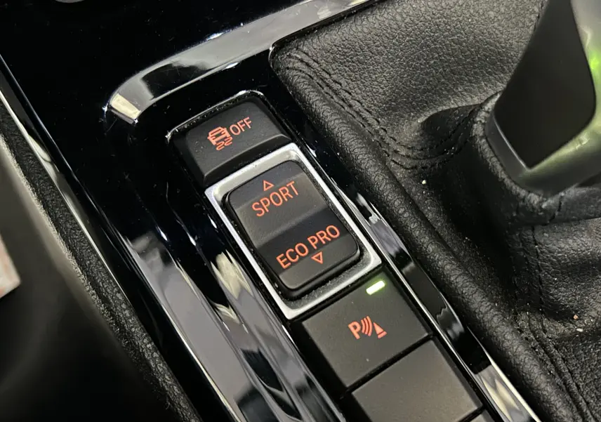 Gros plan sur les commandes de modes de conduite et assistance au stationnement dans l’habitacle d’une BMW X1 gris.