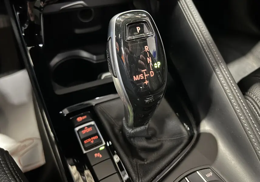 Gros plan sur le levier de vitesses automatique noir brillant et les commandes de mode de conduite dans l’habitacle d’une BMW X1 gris.