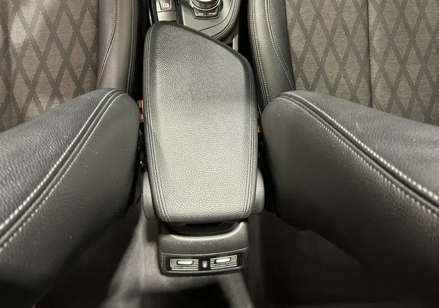 Vue rapprochée de l'accoudoir central en cuir noir entre les sièges avant à motifs du BMW X1 gris.