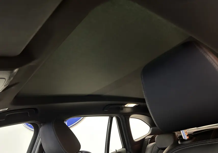 Vue intérieure du toit ouvrant fermé sur BMW X1 gris, avec appuie-tête avant en cuir noir visible.