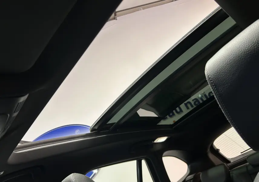 Vue intérieure du toit ouvrant panoramique ouvert sur BMW X1 gris, mettant en valeur les sièges arrière et la lumière ambiante.