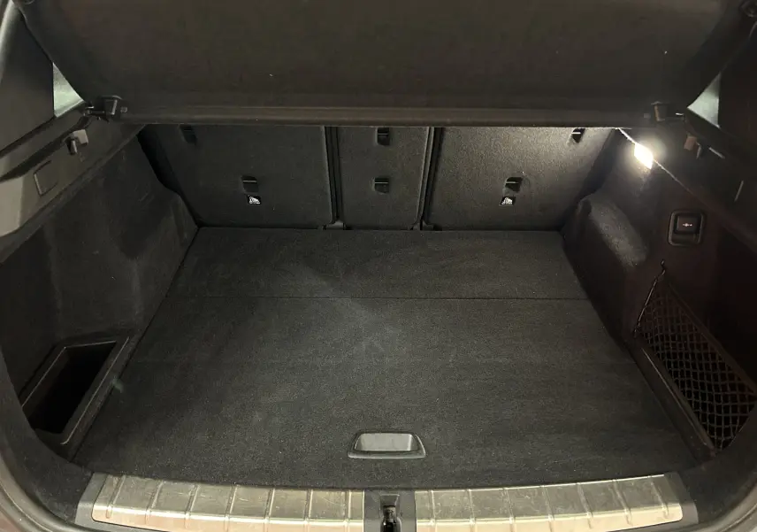 Coffre ouvert de BMW X1 gris, vue intérieure montrant un espace de chargement propre avec éclairage latéral.