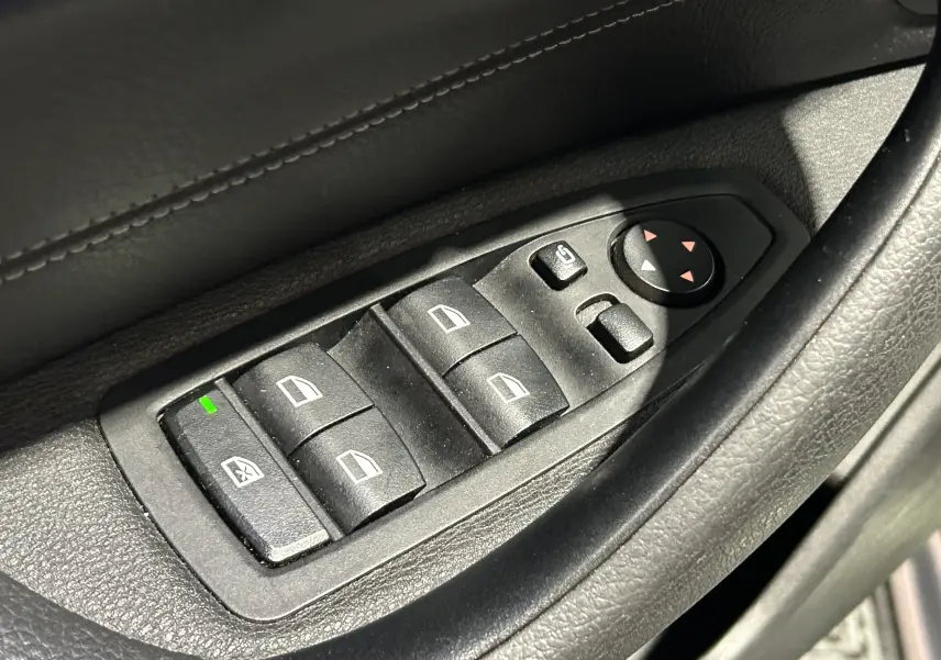Gros plan sur les commandes de lève-vitres et rétroviseurs électriques côté conducteur d’un BMW X1 gris.