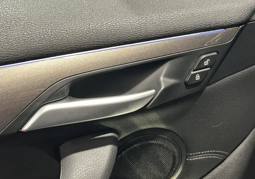 Poignée de porte intérieure côté gauche de BMW X1 gris, avec bouton de verrouillage et finition cuir noire.