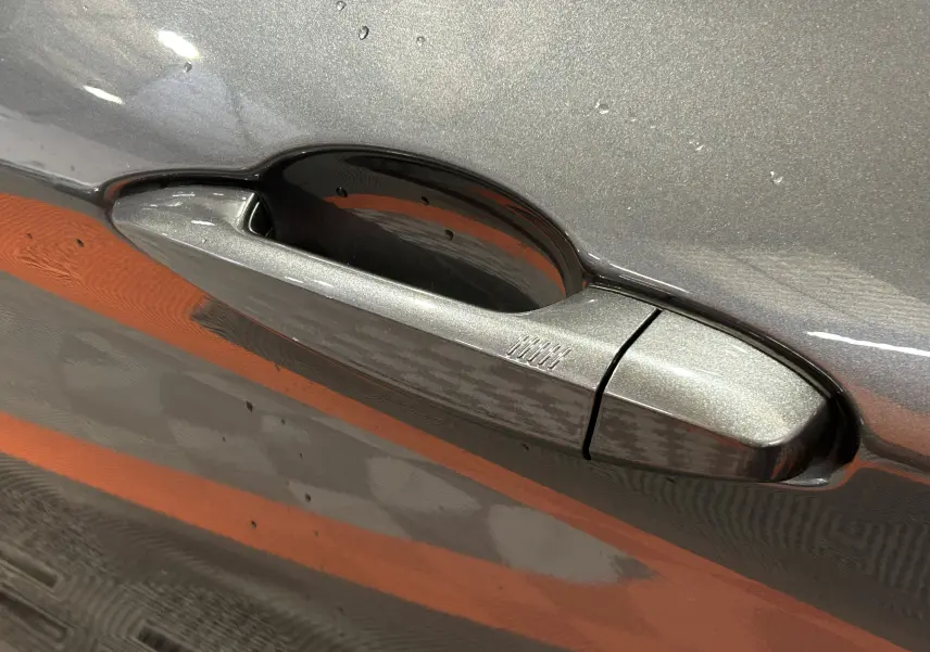 Poignée de porte côté gauche gris métallisé d'une BMW X1 sDrive16d 2021 avec finition lisse et reflet orange.