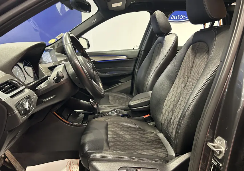 Vue intérieure côté conducteur d’un BMW X1 gris 2021, sièges avant en cuir noir avec surpiqûres et volant multifonction.