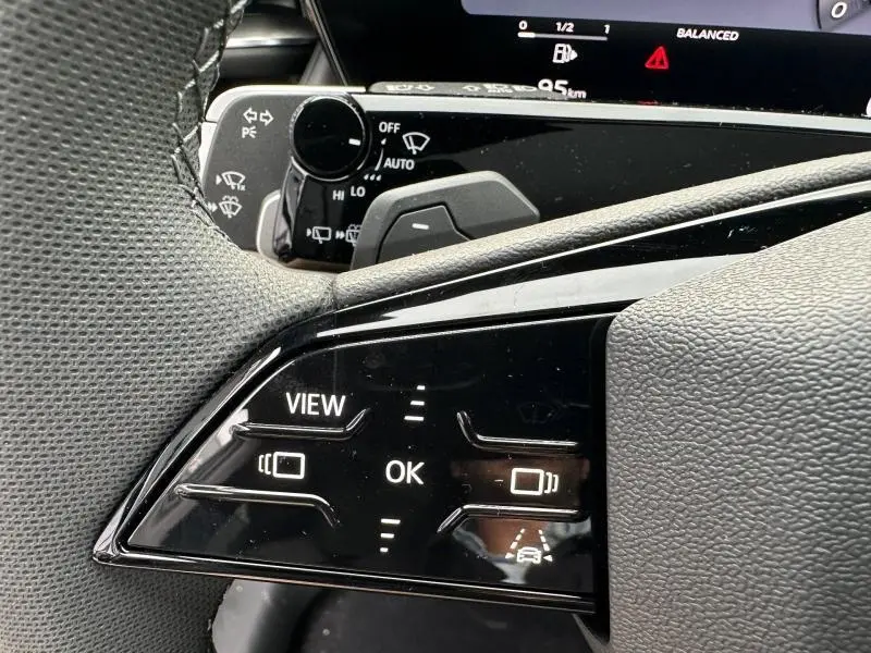 Gros plan sur les commandes au volant noir brillant de l'Audi Q3 2.0 TDI, avec affichage numérique partiel en arrière-plan.