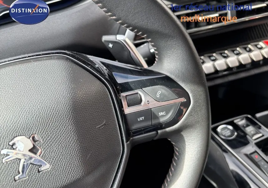 Gros plan sur le volant en cuir noir du Peugeot 3008 Hybrid 2024, avec commandes intégrées et tableau de bord partiel visible.