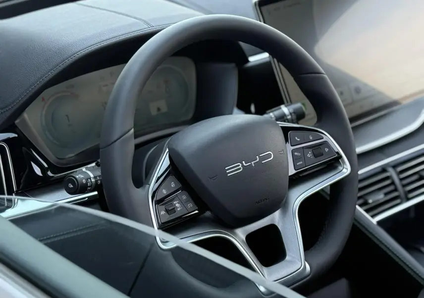 Gros plan sur le volant noir multifonction BYD avec tableau de bord digital et écran tactile à droite.