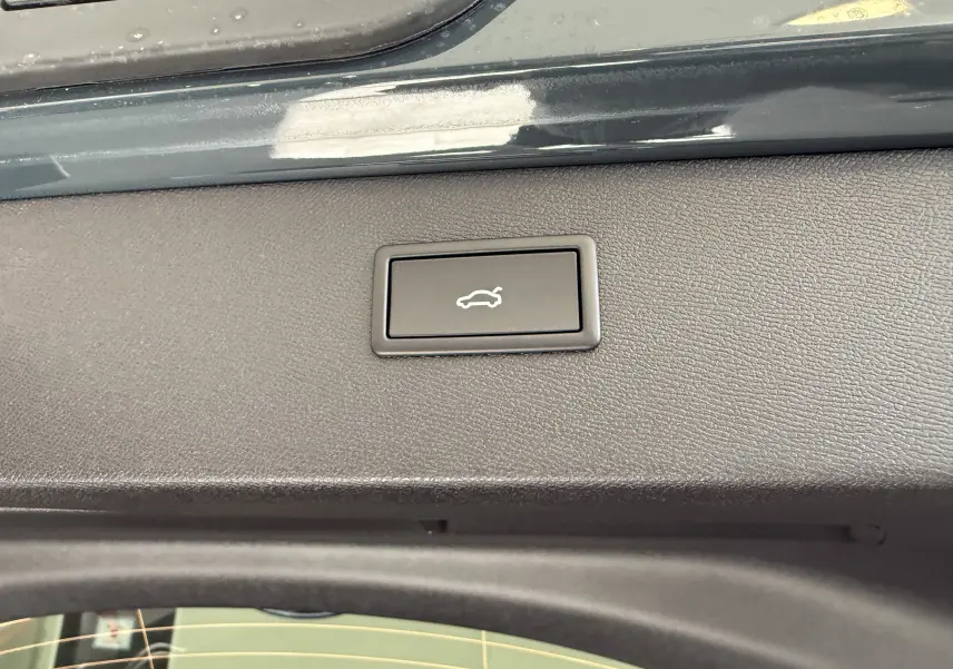 Gros plan sur le bouton d'ouverture électrique du coffre, situé sur la garniture intérieure arrière du CUPRA Formentor gris.