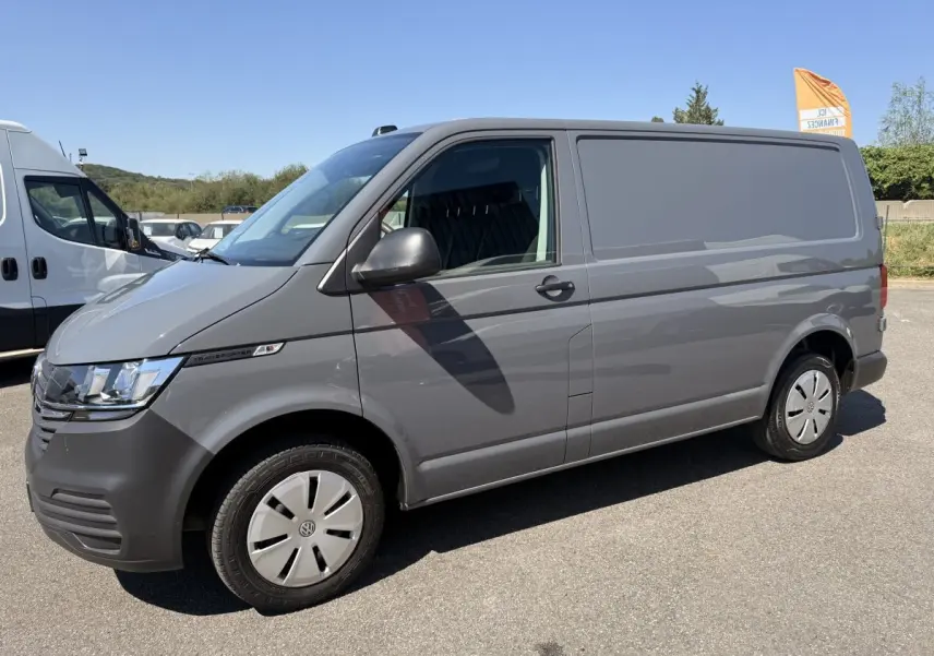 Vue de profil côté gauche d’un Volkswagen Transporter gris clair 2023, fourgon utilitaire avec jantes acier et vitres avant teintées.