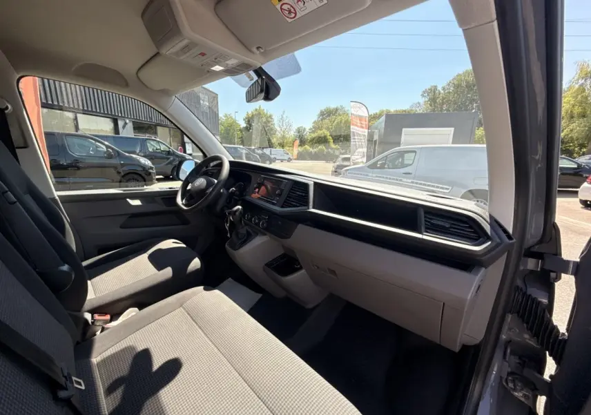 Vue intérieure côté conducteur du Volkswagen Transporter gris clair 2023, mettant en valeur le tableau de bord et les sièges avant.
