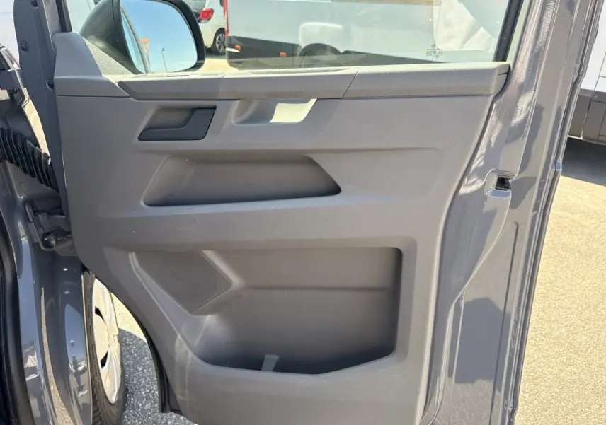 Vue rapprochée de la porte avant gauche gris clair du Volkswagen Transporter 2023 avec rétroviseur électrique et rangement intégré.