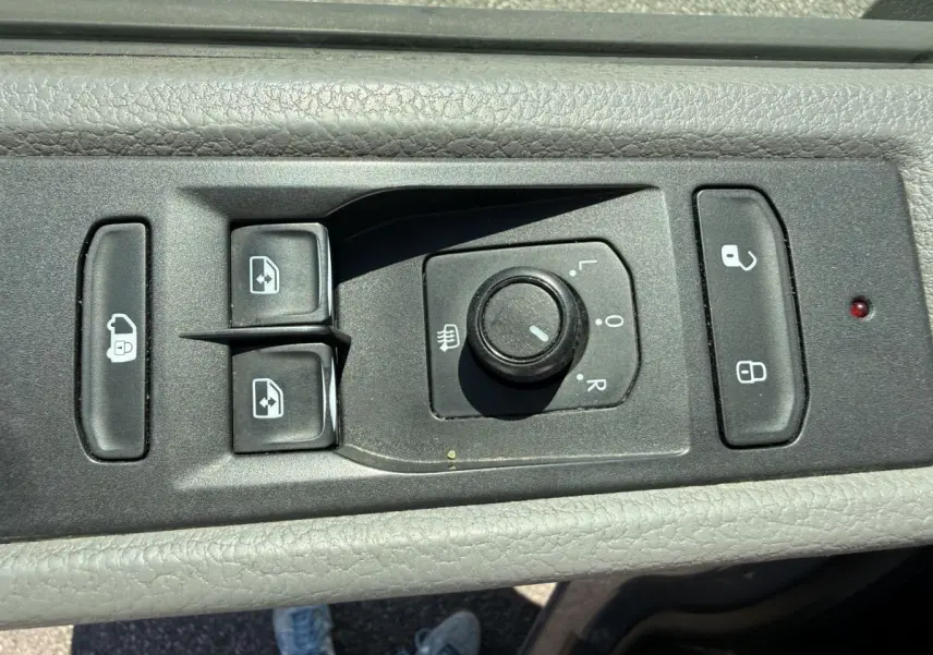 Gros plan sur les commandes de réglage des rétroviseurs et des vitres côté conducteur du Volkswagen Transporter gris clair 2023.