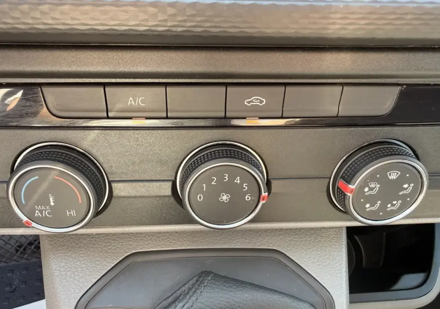 Gros plan sur les commandes de climatisation du Volkswagen Transporter gris clair, avec boutons rotatifs et touches A/C et recyclage d'air.