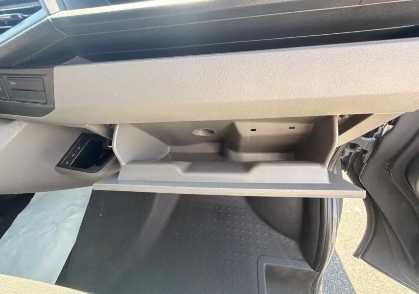 Vue intérieure côté passager du Volkswagen Transporter gris clair 2023, boîte auto, avec boîte à gants ouverte et plancher visible.