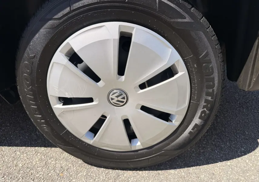 Gros plan sur la roue avant droite du Volkswagen Transporter gris clair, avec enjoliveur argenté et logo VW central.