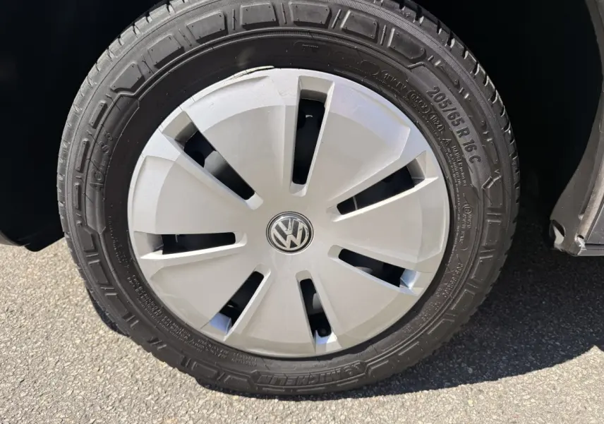 Gros plan sur la roue avant droite du Volkswagen Transporter gris clair, avec enjoliveur argenté et logo VW central.