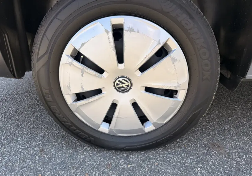 Gros plan sur la roue avant droite du Volkswagen Transporter gris clair, avec enjoliveur marqué du logo VW.