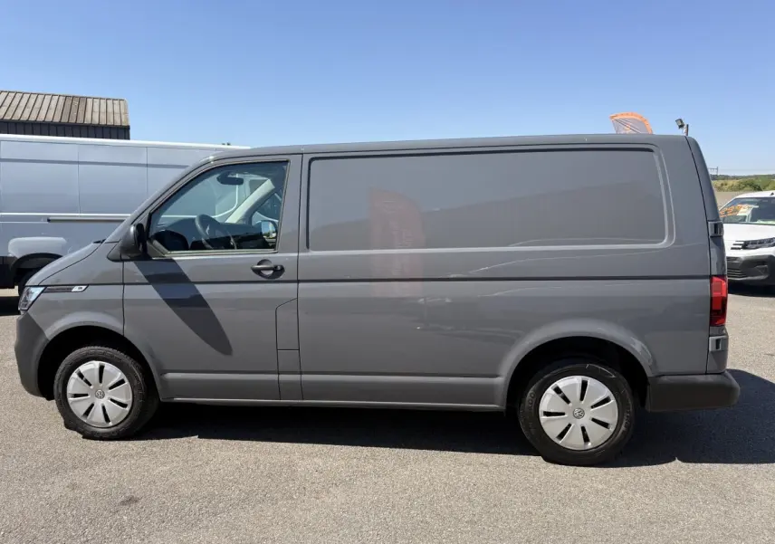 Vue de profil côté gauche d’un Volkswagen Transporter gris clair 2023, fourgon utilitaire avec jantes acier et vitres teintées.