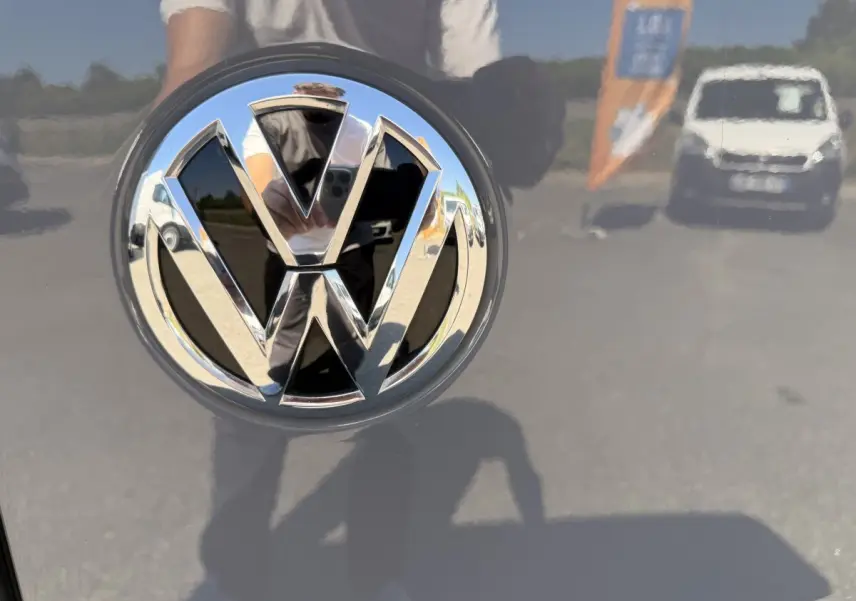 Gros plan sur le logo chromé Volkswagen sur la porte arrière d’un Volkswagen Transporter gris clair 2023.
