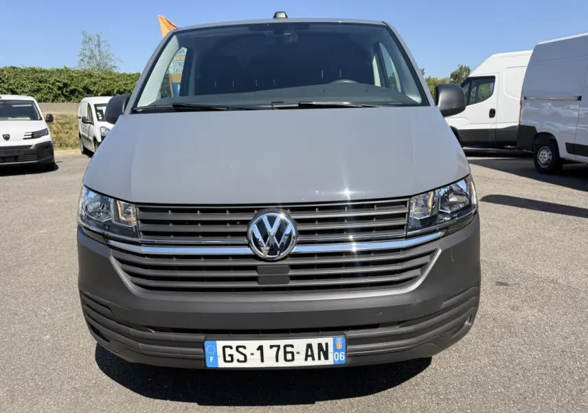 Vue de face d'un Volkswagen Transporter gris clair 2023 avec calandre chromée et plaque d'immatriculation française.