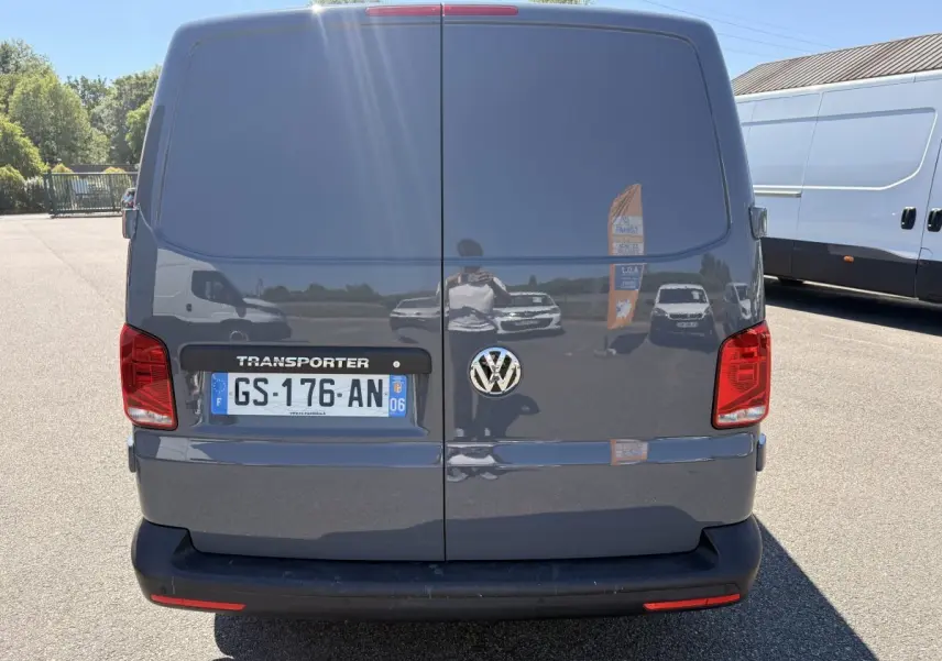 Vue arrière d’un Volkswagen Transporter gris clair 2023 avec portes battantes et feux rouges visibles.