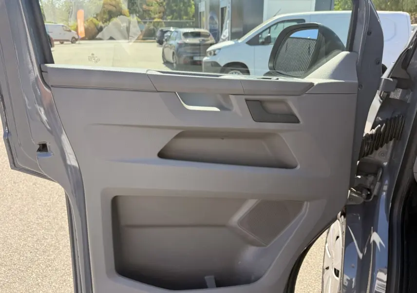 Vue rapprochée de la porte avant droite gris clair du Volkswagen Transporter 2023, avec poignée et haut-parleur intégrés.