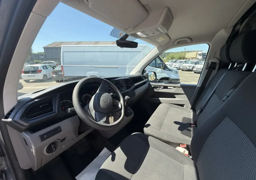 Vue intérieure côté conducteur du Volkswagen Transporter gris clair 2023, montrant le tableau de bord et les sièges avant.