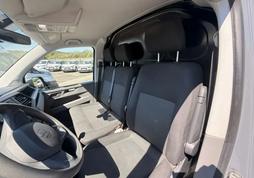 Vue intérieure côté conducteur du Volkswagen Transporter gris clair 2023, montrant les sièges avant et le tableau de bord.