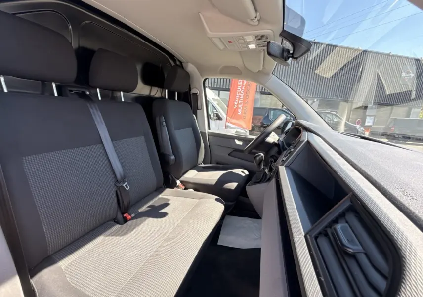 Vue intérieure côté conducteur du Volkswagen Transporter 2023, sièges tissu gris et tableau de bord noir.