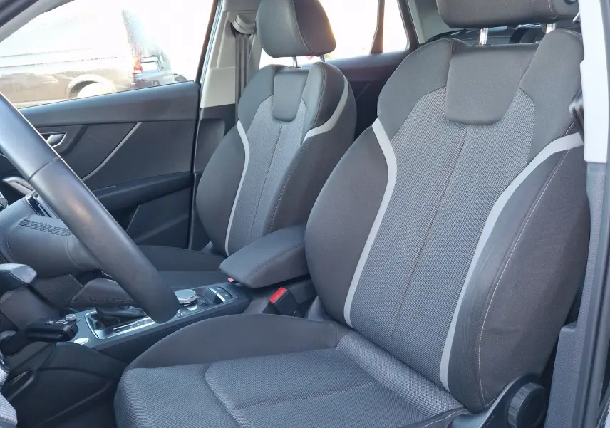 Vue intérieure côté conducteur de l'Audi Q2 35 TFSI 2021 noire, sièges sport en tissu gris avec surpiqûres claires.