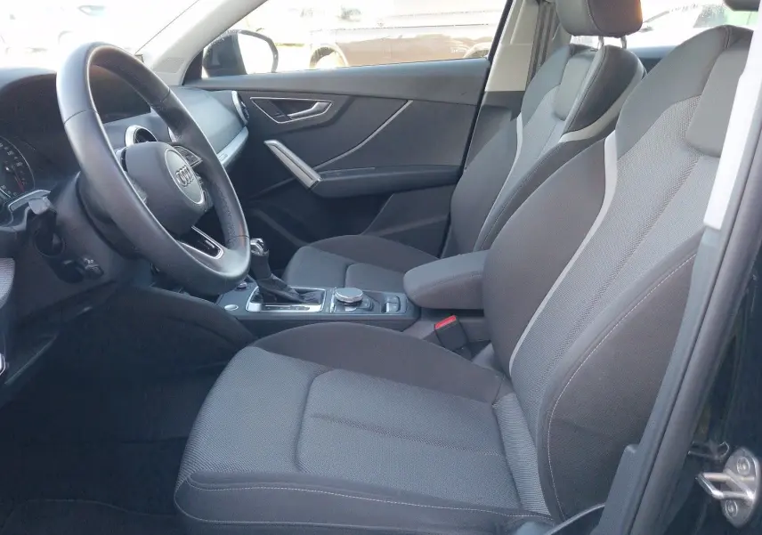 Vue intérieure côté conducteur de l'Audi Q2 noire, montrant sièges en tissu et tableau de bord moderne.