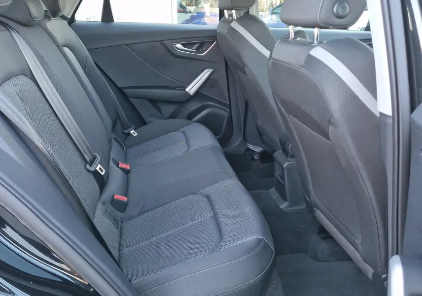 Vue intérieure arrière côté gauche de l'Audi Q2 noire, montrant les sièges arrière en tissu et les appuie-têtes réglables.