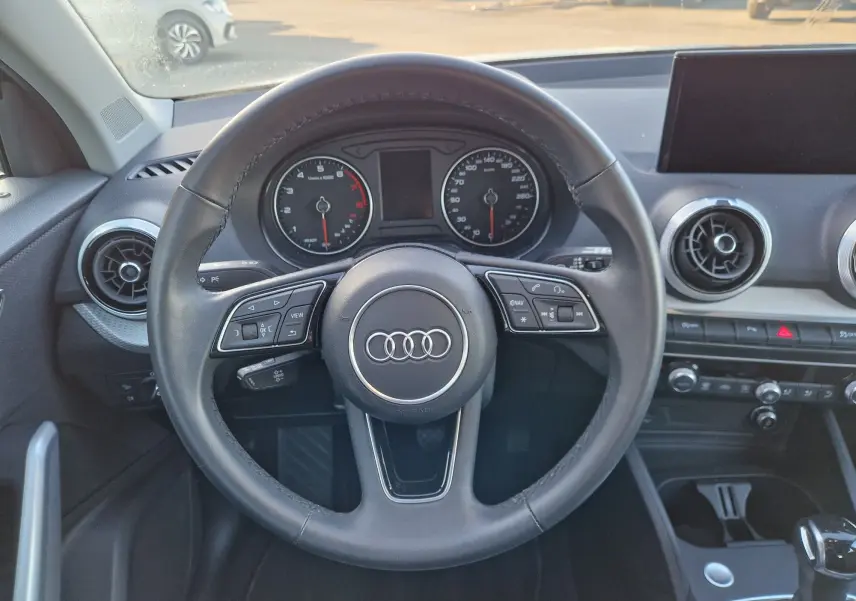 Vue intérieure centrée sur le volant cuir noir de l'Audi Q2 2021, avec tableau de bord et aérateurs ronds visibles.