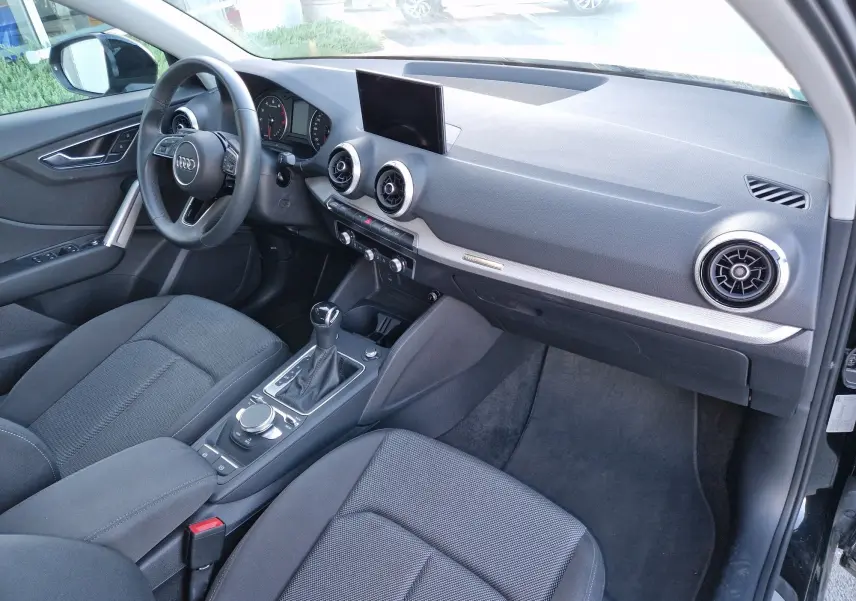 Vue intérieure côté conducteur de l'Audi Q2 noire, mettant en valeur le tableau de bord moderne et la console centrale.