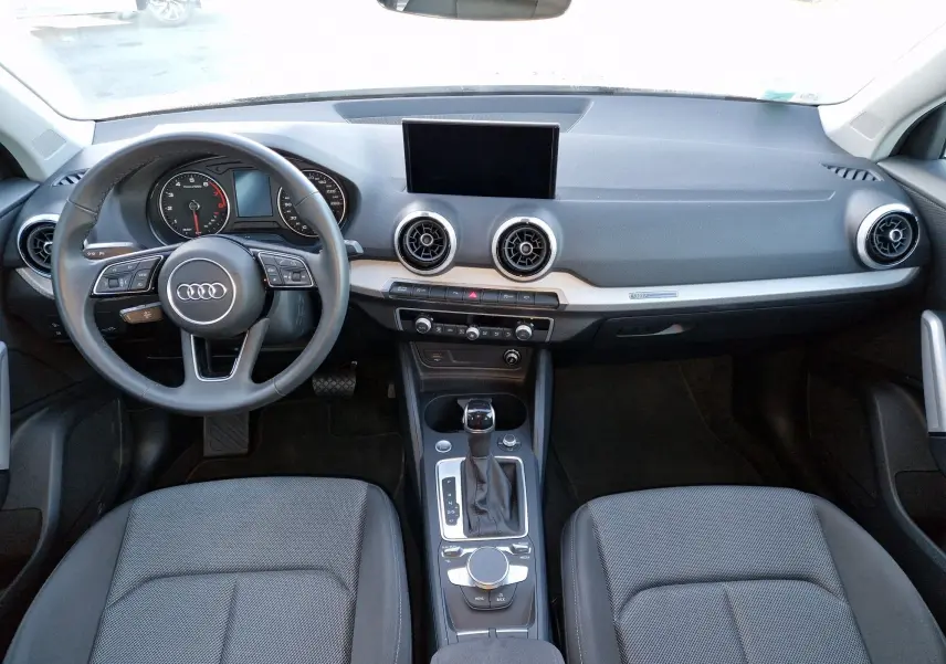 Vue intérieure avant de l'Audi Q2 35 TFSI noir, montrant le tableau de bord moderne avec écran central et volant multifonction.