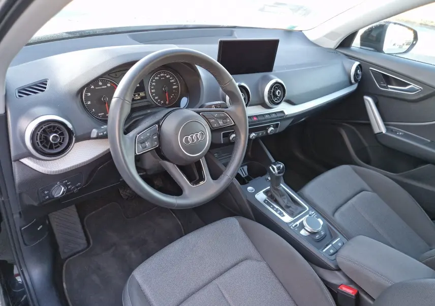 Vue intérieure de l'Audi Q2 35 TFSI 2021, côté conducteur, avec tableau de bord noir et écran central déployé.
