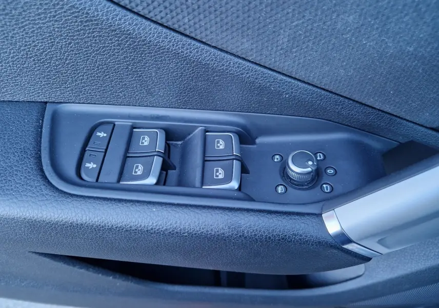 Gros plan sur les commandes de lève-vitres et réglage des rétroviseurs côté gauche d’un Audi Q2 noir.