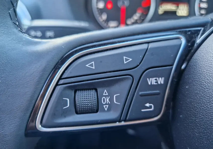 Gros plan sur les commandes multifonctions noires à gauche du volant de l'Audi Q2 35 TFSI 2021, avec boutons fléchés et molette.