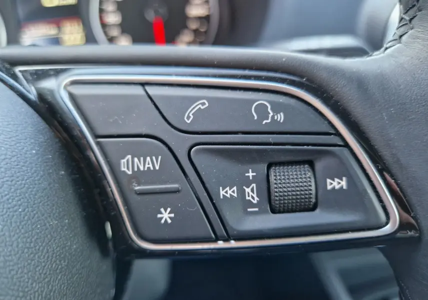 Gros plan sur les commandes du volant côté gauche de l’Audi Q2 noir, avec boutons navigation, appel et volume.