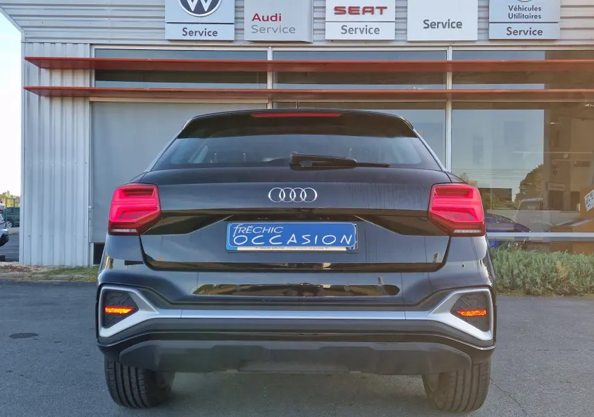 Vue arrière d'un Audi Q2 noir 2021 avec feux LED et plaque d'occasion visible devant un garage multimarque.